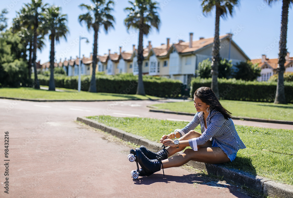 Spain, Gijon, teenage girl sitting on curb tying her roller skates ...