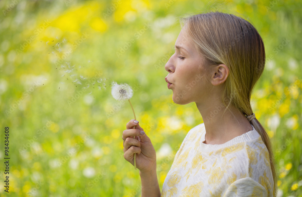 Portrait of teenage girl blowing dandelion on a flower meadow Portrait of teenage girl blowing dandelion on a flower meadow
