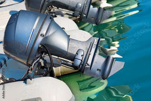 Two Outboard Boat Motors / Detail of two outboard used engines, on an inflatable boat on the water with reflections photo