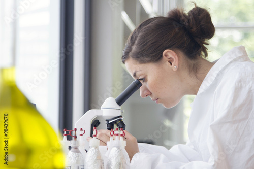 Portrait of young female chemist looking through microscope