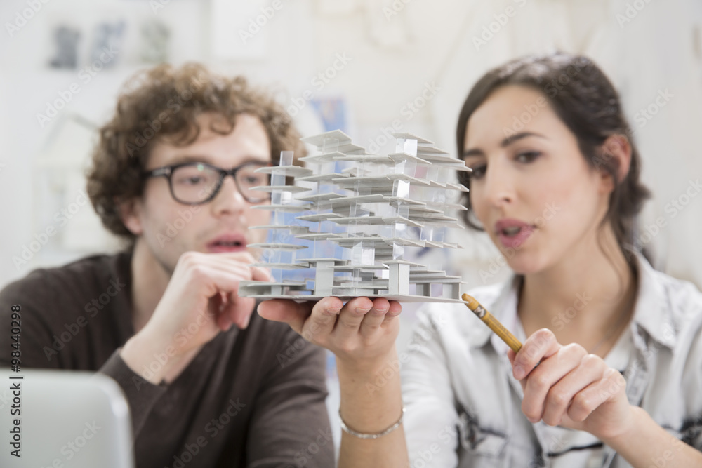 Portrait of two young architects looking at architectural model in office Portrait of two young architects looking at architectural model in office