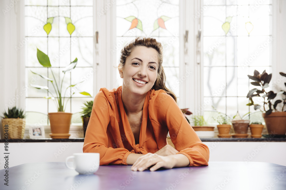 Portrait of smiling young woman sitting at blue table at home Portrait of smiling young woman sitting at blue table at home