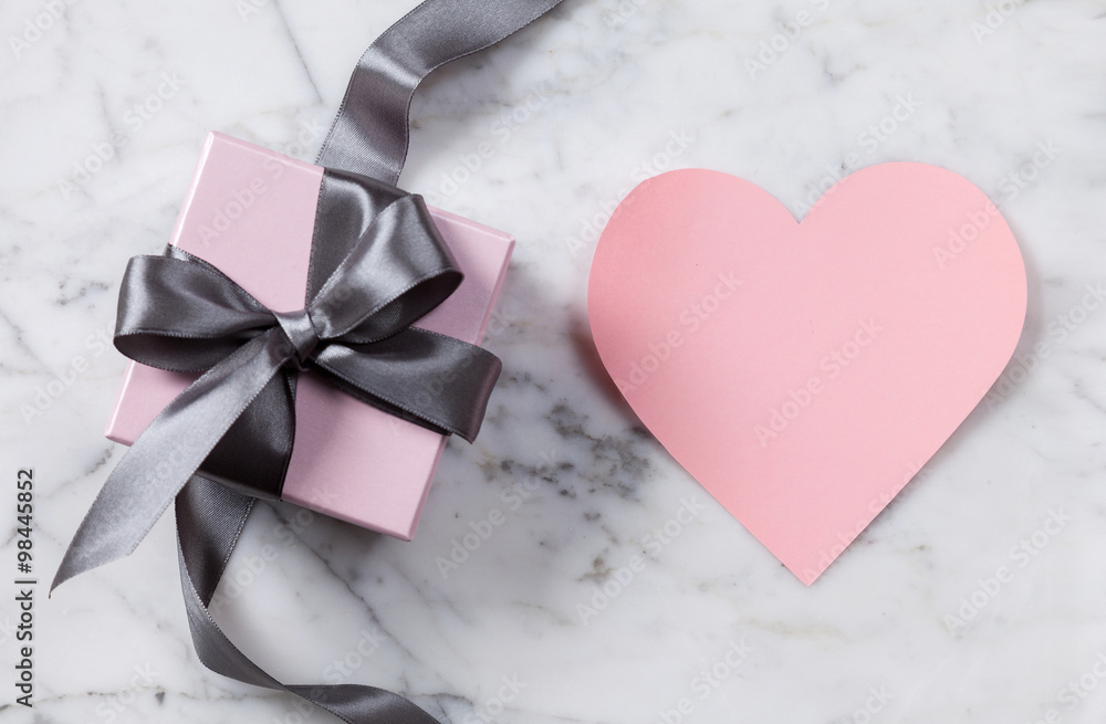 Pink heart and gift box with a gray silk ribbon and bow on a marble background