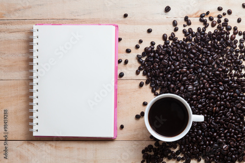 a cup coffee of black coffee with beans and note book on woo