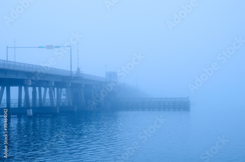 A draw bridge with stop light, gate, bridge keeper's house and channel bumpers is disappearing into a heavy fog. © Michael O'Keene
