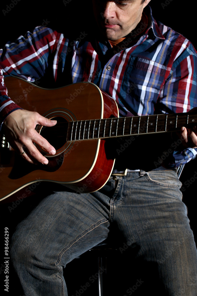 Fototapeta Mann spielt bei Konzertbeleuchtung Gitarre, schwarzer Hintergrund