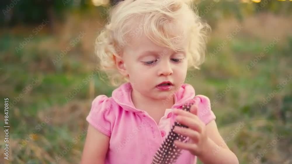A cute little girl playing with a feather in a field A cute little girl playing with a feather in a field