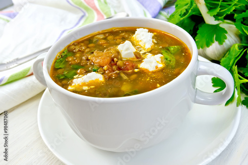 Soup lentil with spinach and feta in white cup on board