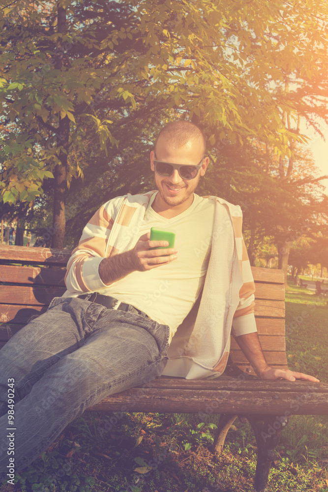Obraz premium Urban guy texting on a bench in the park.