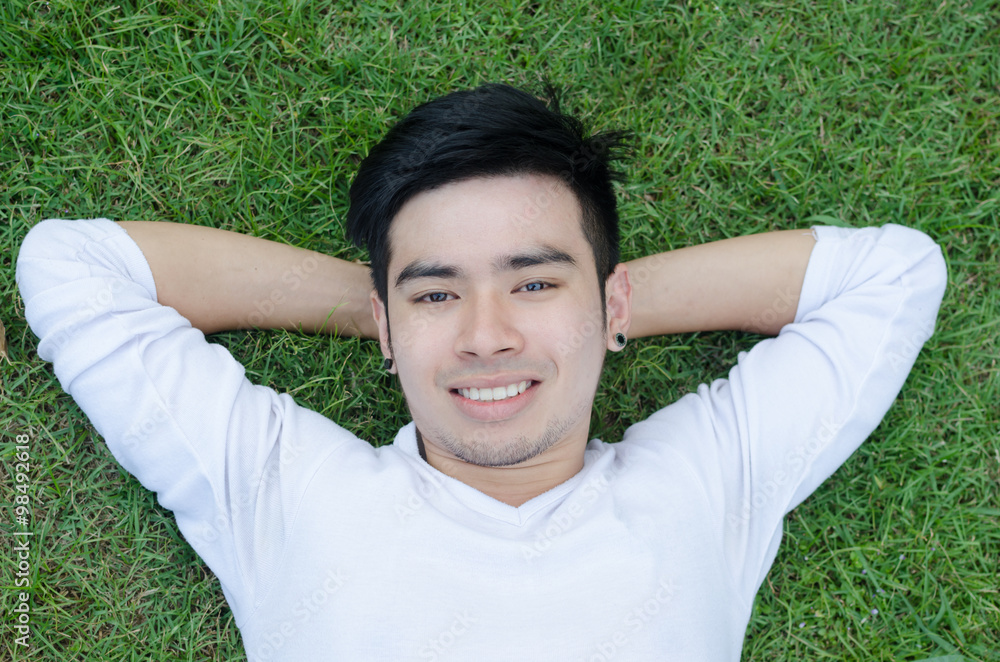 Portrait of a young happy man relaxing on the grass with his han Portrait of a young happy man relaxing on the grass with his han