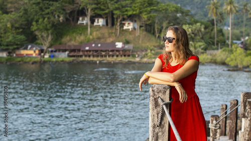 Spectacular girl in a red dress looks at water of tropical lagoon. © De Visu