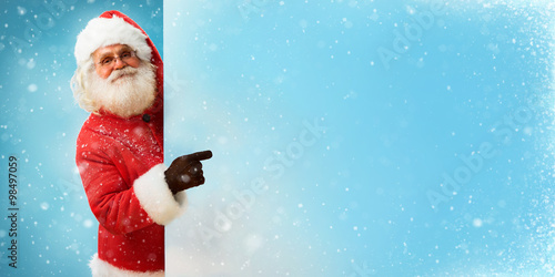 Santa Claus holding banner with blue space for Your Text / Merry Christmas & New Year's Eve concept / Closeup on blurred blue background. © Romario Ien