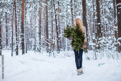 girl dressed in a sweater keeps fir branches in the winter forest