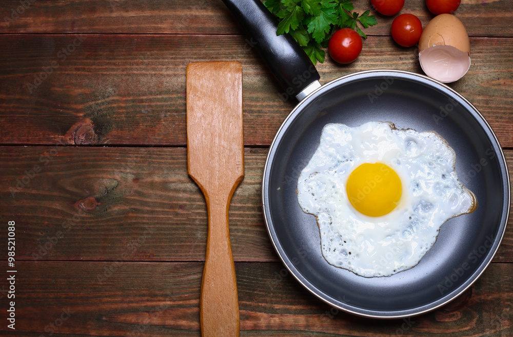 Pan of fried eggs, with cherry-tomatoes and parsley on a wooden table surface Pan of fried eggs, with cherry-tomatoes and parsley on a wooden table surface