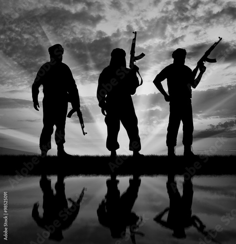 Silhouette of men with rifle standing against cloudy sky with reflection in water