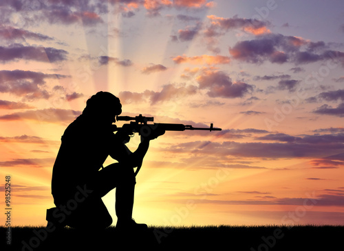 Silhouette of man with rifle against cloudy sky during sunset