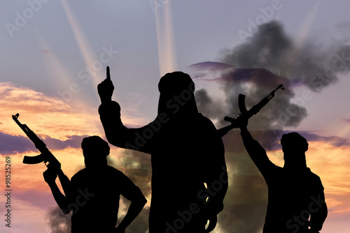 Silhouette of men with rifles against cloudy sky during sunset