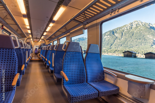 Image with the interior of a german border train, with comfortable modern chairs and a mountain landscape viewed through the window. 