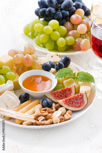 cheeses, fruits, wine and snacks on plate, vertical closeup