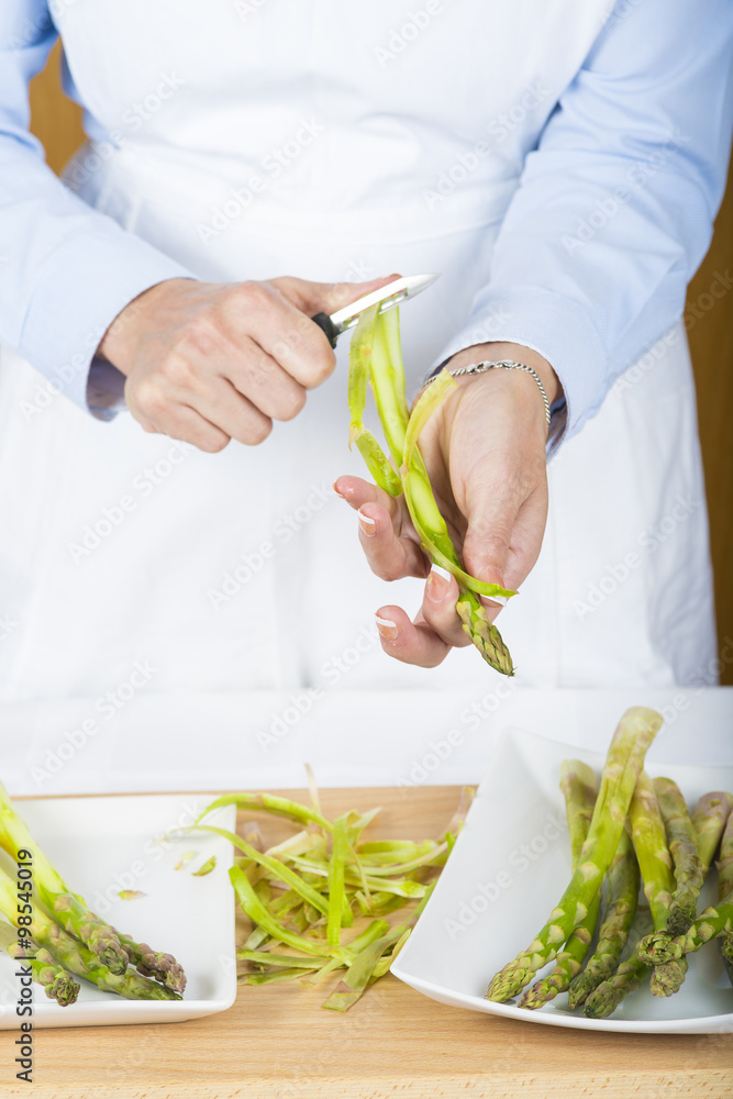 Gente trabajando como cocinero pelando y cortando espárragos trigueros verdes frescos en la mesa de la cocina Gente trabajando como cocinero pelando y cortando espárragos trigueros verdes frescos en la mesa de la cocina