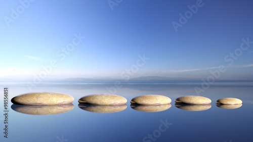 Photo Zen stones row from large to small  in water with blue sky and peaceful landscap