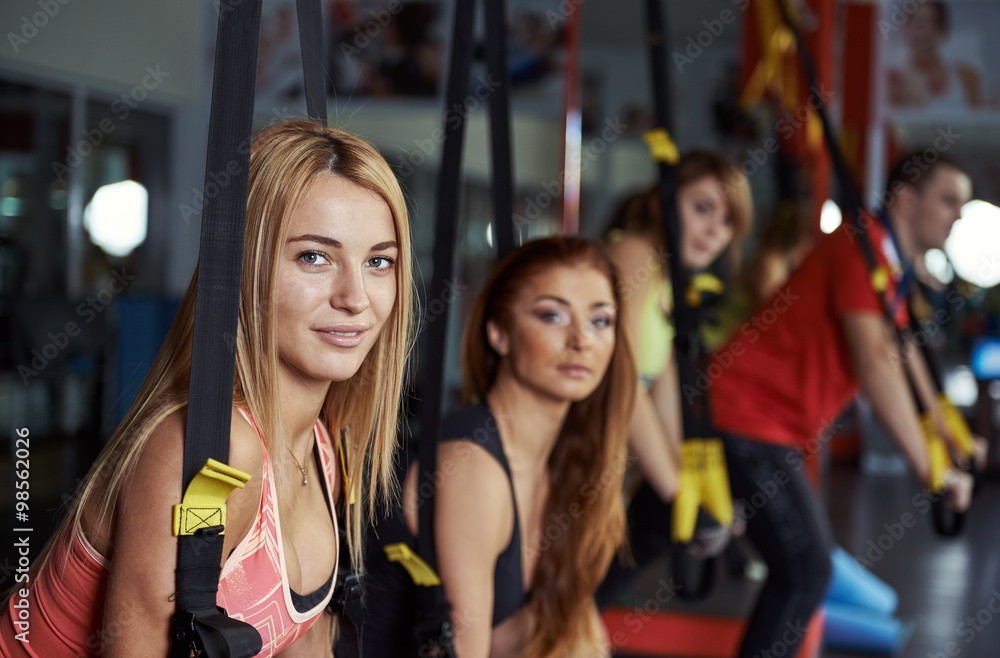 Fitness team doing stretching exercise holding band in the gym. Young active people training arms muscles with elastic rope in sport club. Fitness team doing stretching exercise holding band in the gym. Young active people training arms muscles with elastic rope in sport club.