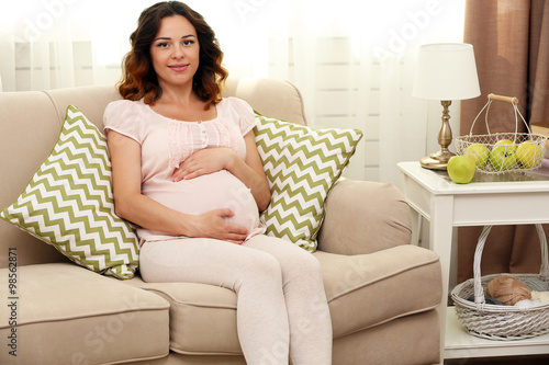 Cute happy pregnant woman on sofa in the room