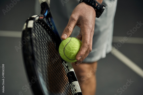 Close-up of male hand holding tennis ball and racket. Professional tennis player starting set.  © Stasique