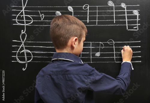 Fotografie Cute boy writing at the blackboard with musical notes, in the classroom