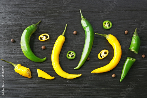 Green and yellow chili peppers on dark wooden background