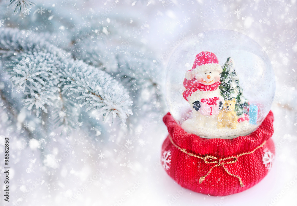 A snow globe with snowman on a background snow-covered fir branches A snow globe with snowman on a background snow-covered fir branches