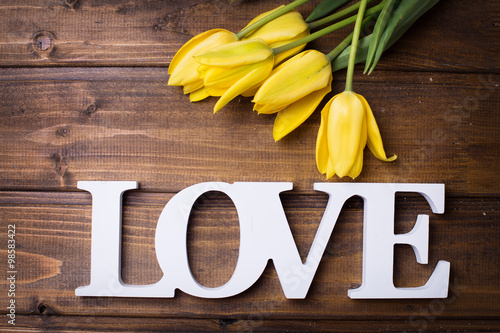 Fototapeta Naklejka Na Ścianę i Meble -  Fresh spring yellow tulips  flowers and word love on dark  woode