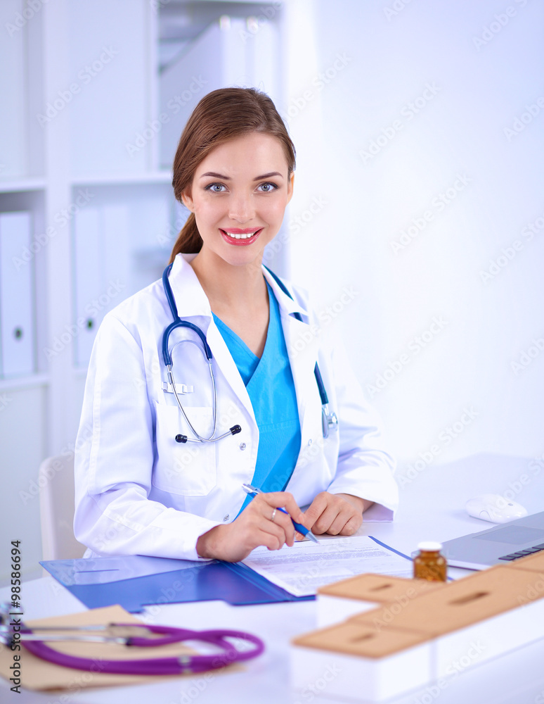 Beautiful young smiling female doctor sitting at the desk and writing Beautiful young smiling female doctor sitting at the desk and writing