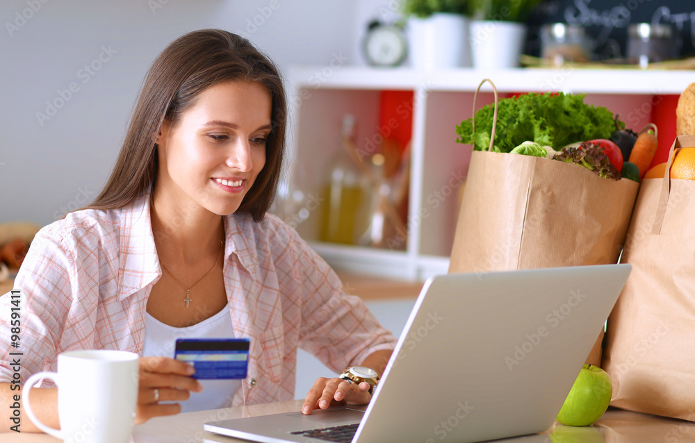 Smiling woman online shopping using tablet and credit card in kitchen Smiling woman online shopping using tablet and credit card in kitchen