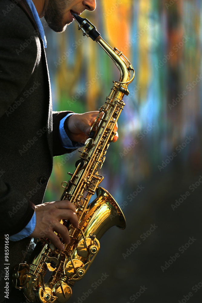 Fototapeta premium Young man with saxophone outside near the old painted wall