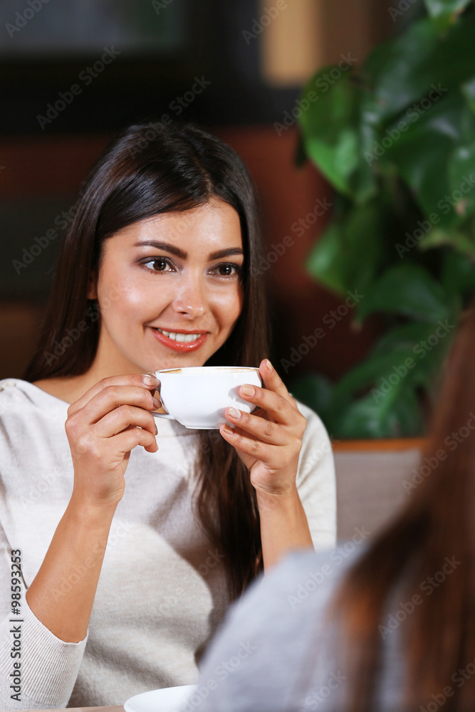 Beautiful girls drink coffee and speaking in cafe Beautiful girls drink coffee and speaking in cafe