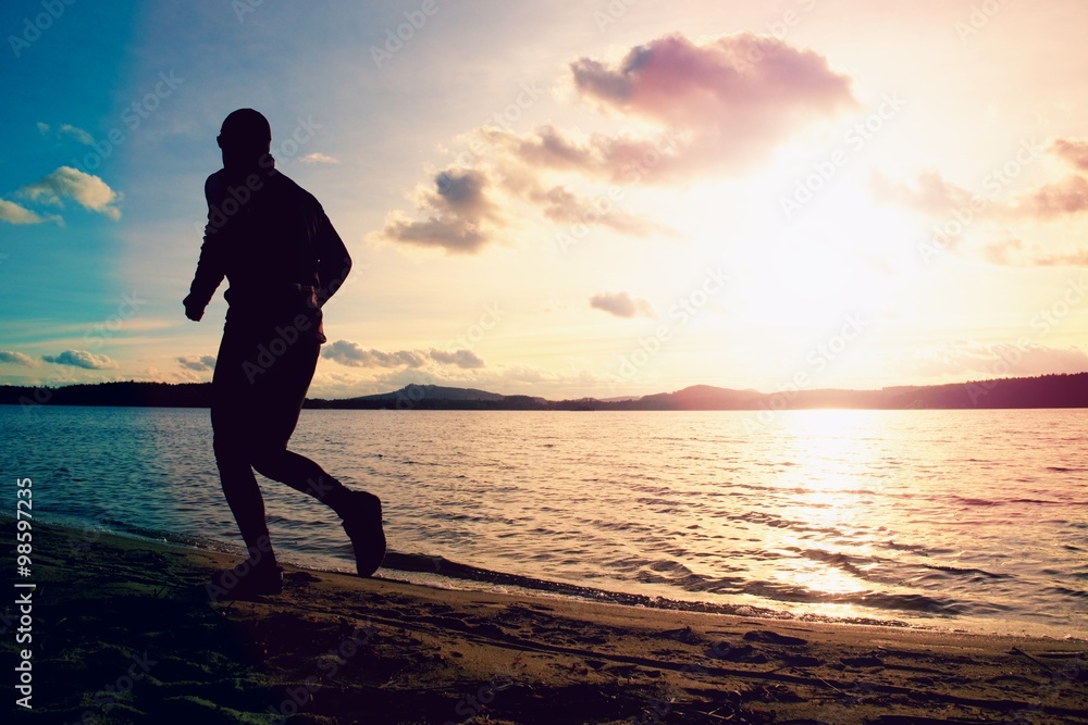 Silhouette of sport active man running on evening  beach water mountain and sunset cloudy sky background.