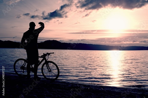 Young man cyclist silhouette on blue sky and sunset above the beach. Biker atthe end of season at lake. © rdonar