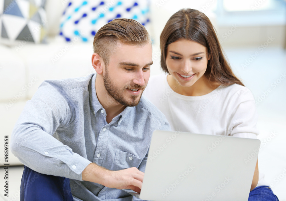 Happy couple sitting on the floor and working on laptop in a room Happy couple sitting on the floor and working on laptop in a room