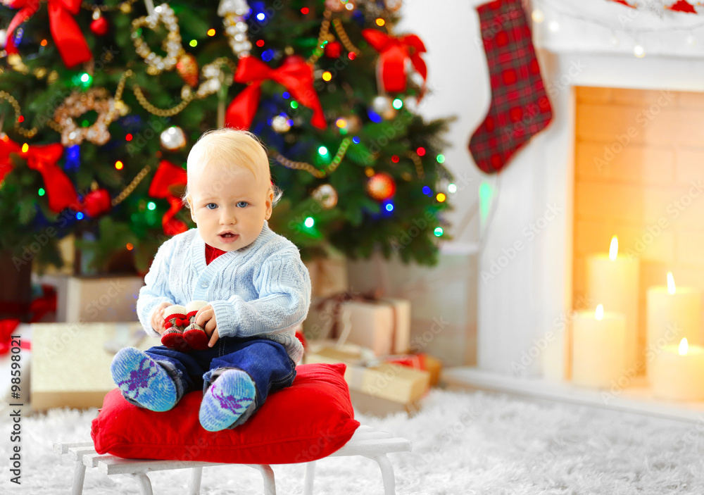 Funny baby sitting on sledge and Christmas tree and fireplace on background Funny baby sitting on sledge and Christmas tree and fireplace on background