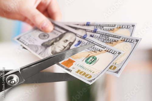 Hands with scissors cutting dollar banknotes, on blurred interior background