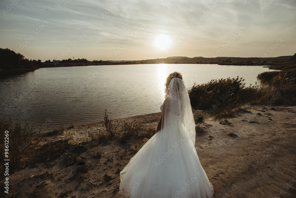 bride looking at the amazing sunset on a background of beautiful sunny lake and sand bride looking at the amazing sunset on a background of beautiful sunny lake and sand