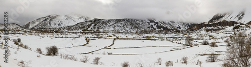 Panorama de Paisaje Montañoso con Nieve - Vista panoramica de paisaje montañoso con nieve en invierno y llanura en primer plano. Con nubes bajas cayendo sobre las crestas y praderas en primer plano