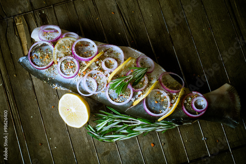 Fish Nelma with lemon, onion and rosemary on a wooden table. Ton photo