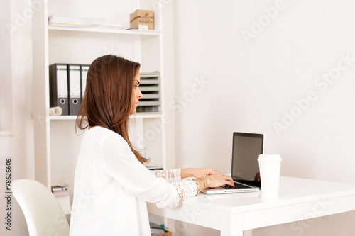 Junge Frau im Büro mit Getränkebecher vor Laptop © Peter Atkins