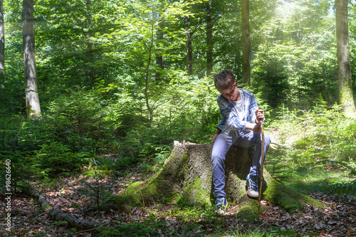 Young boy uses a knife to whittle a stick while out hiking in th