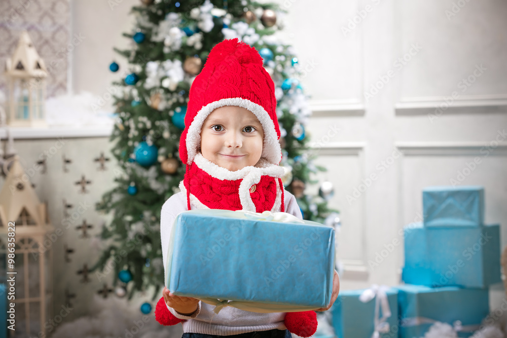 Cute little boy holding a gift against Christmas tree in background