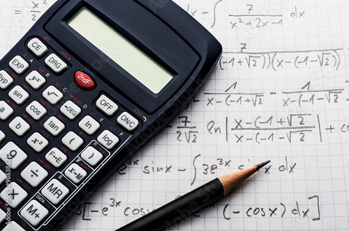 Maths concept - handheld calculator and pencil over a sheet of paper with maths-formulas