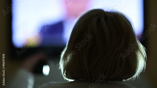 Woman with remote control switching tv channels. Back of the head photo