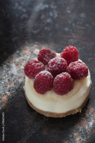 Closeup of an individual raspberry cheesecake on a dark granite counter top
